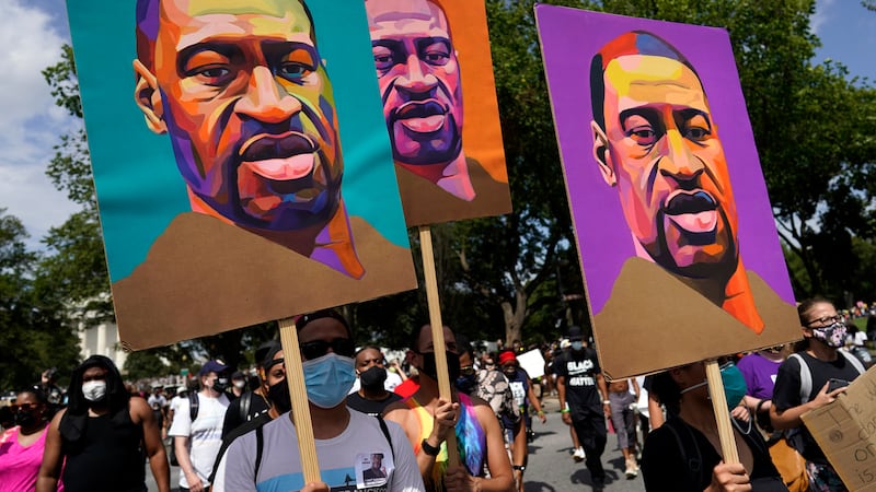 FILE - In this Aug. 28, 2020, file photo, people carry posters with George Floyd on them as...